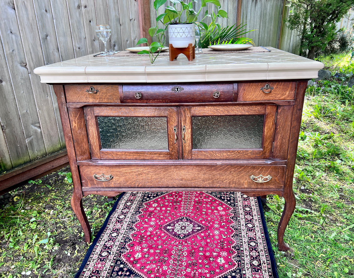 This is a unique antique wooden hutch with a cream colored tiled top that could used as a kitchen island